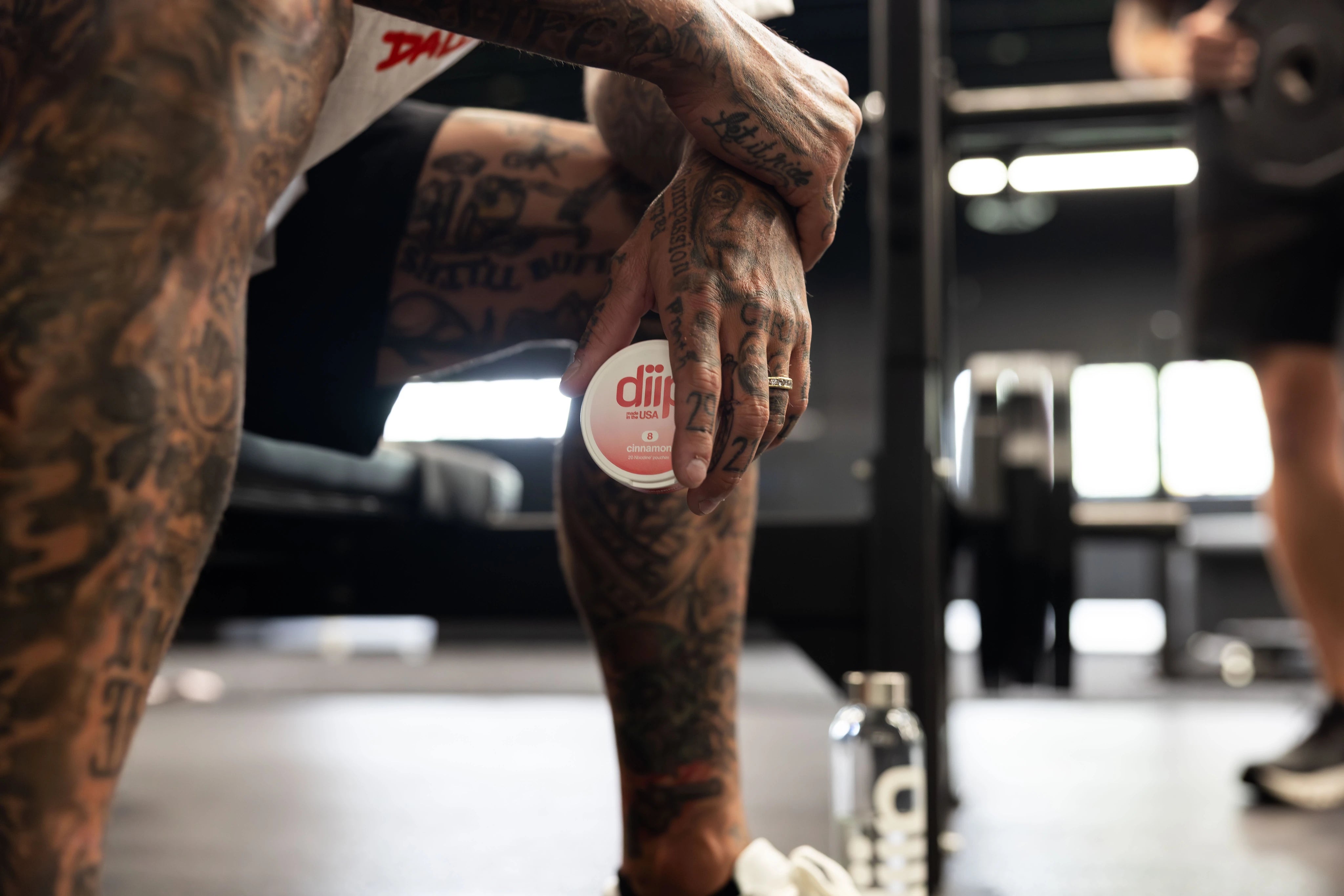 A close-up shot of Ryan Sheckler sitting on a bench holding a 'diip' branded 8 cinnamon nicotine-free dip pouch can