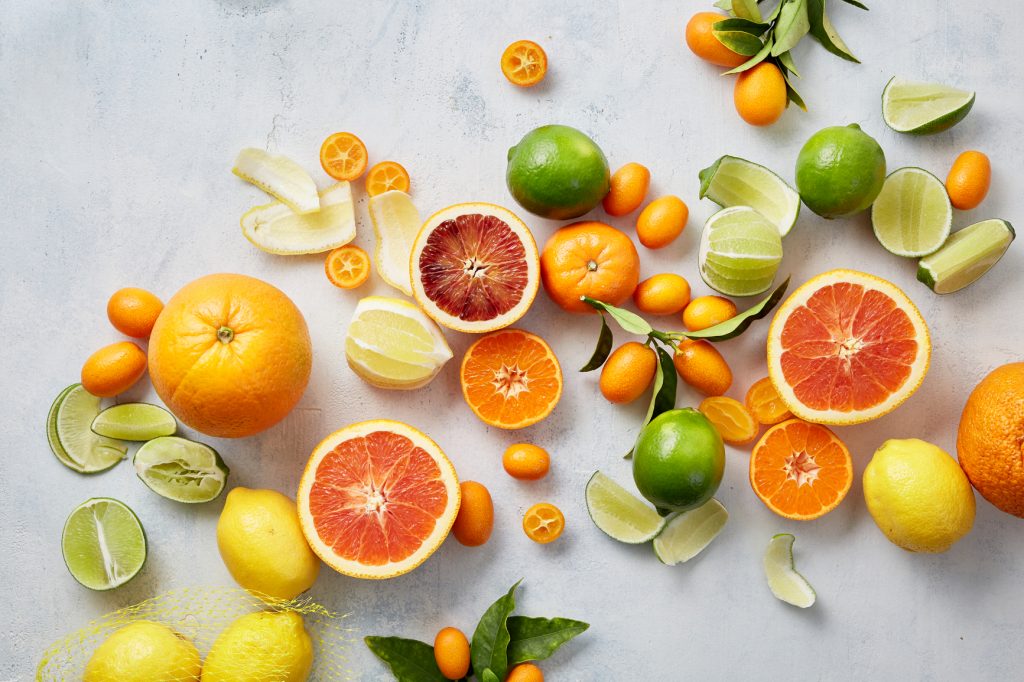 Assorted citrus fruits including oranges, lemons, and limes on a light gray background
