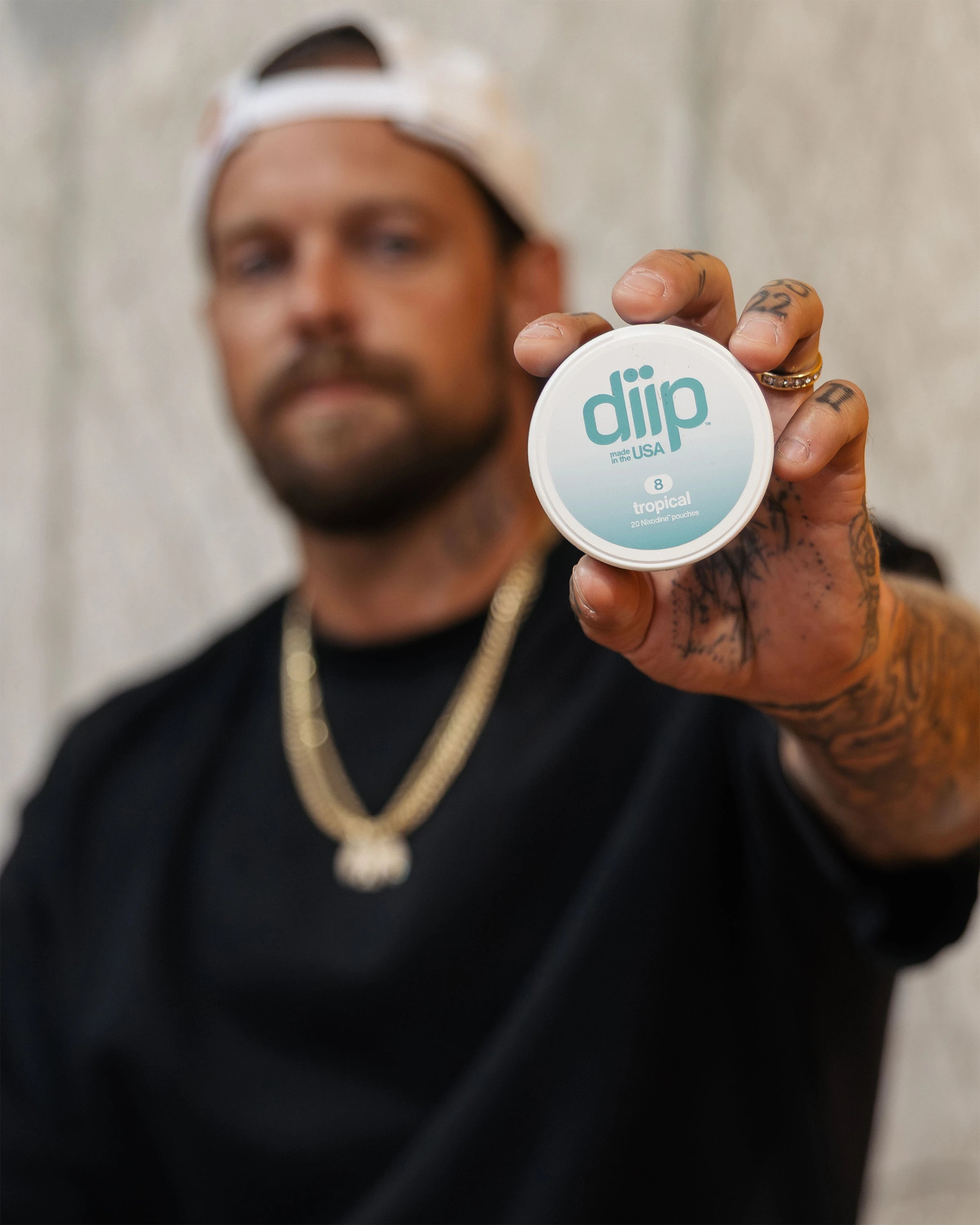 Ryan Sheckler holding a 'diip' branded 8 tropical nicotine-free dip pouch can against a neutral background