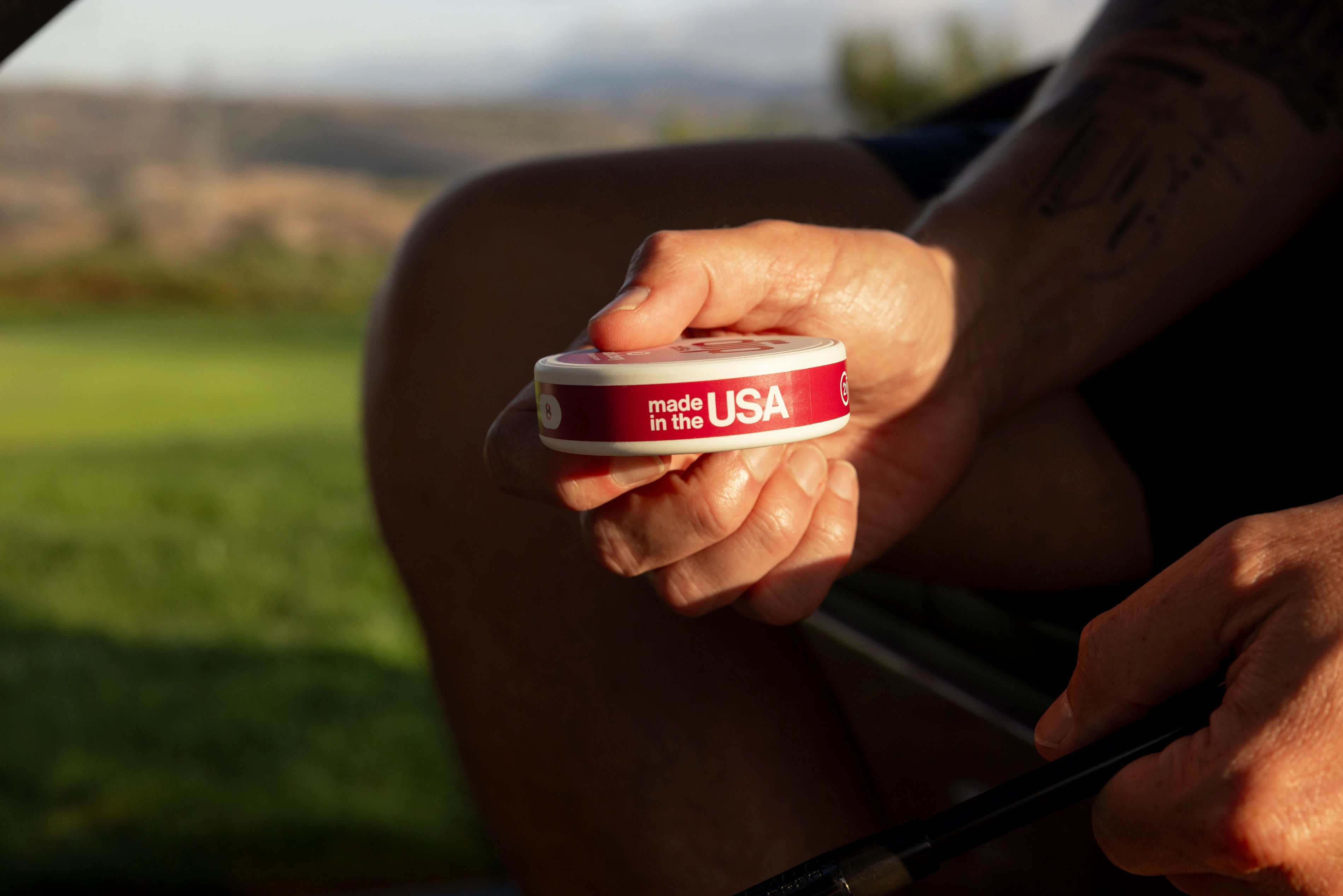 Person holding a 'diip' branded nicotine-free dip pouch can labeled 'made in the USA' with a blurred natural background