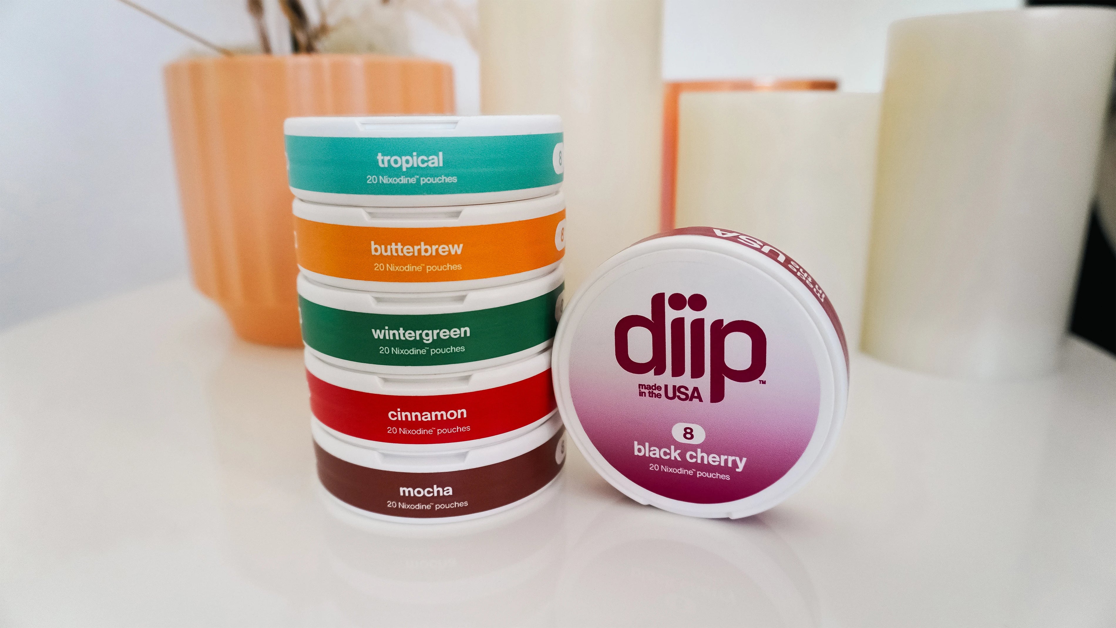 Stack of 6 'diip' branded nicotine-free  dip pouch cans on a side table with candle and potted plant