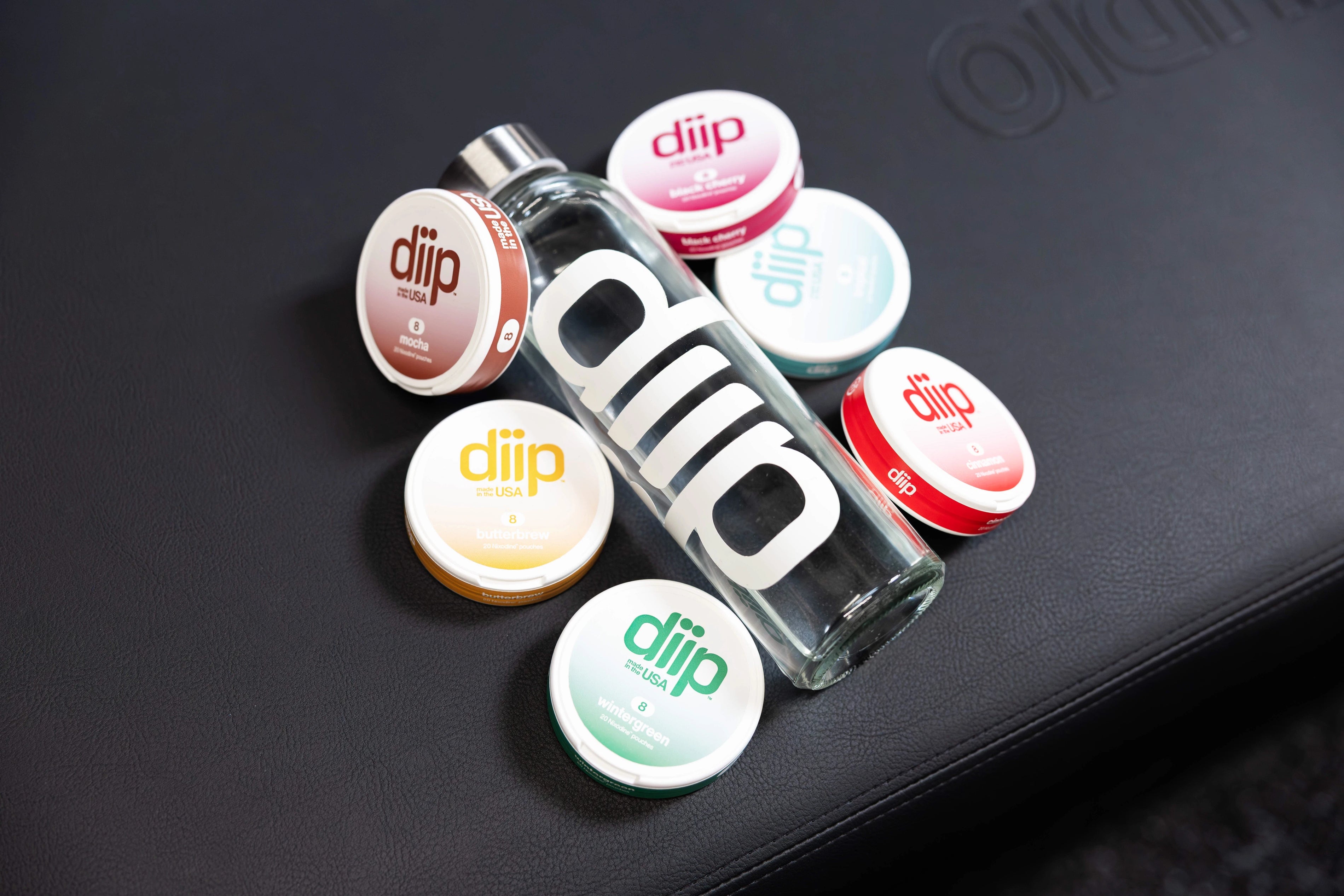 Stack of 6 'diip' branded nicotine-free  dip pouch cans on a side table with candle and potted plant