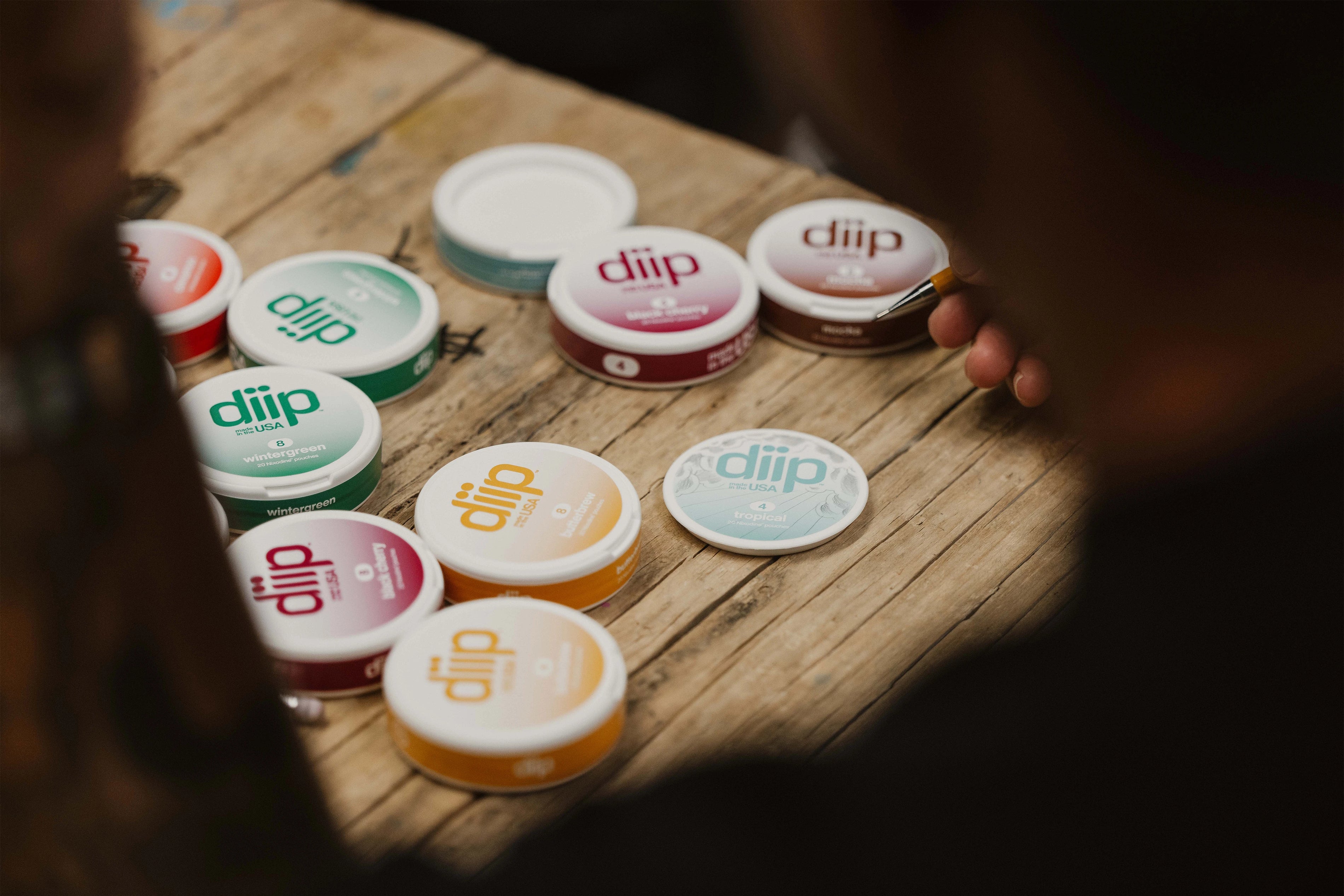 Collection of 'diip' branded nicotine-free dip pouch cans getting drawn on on top of a wooden surface 