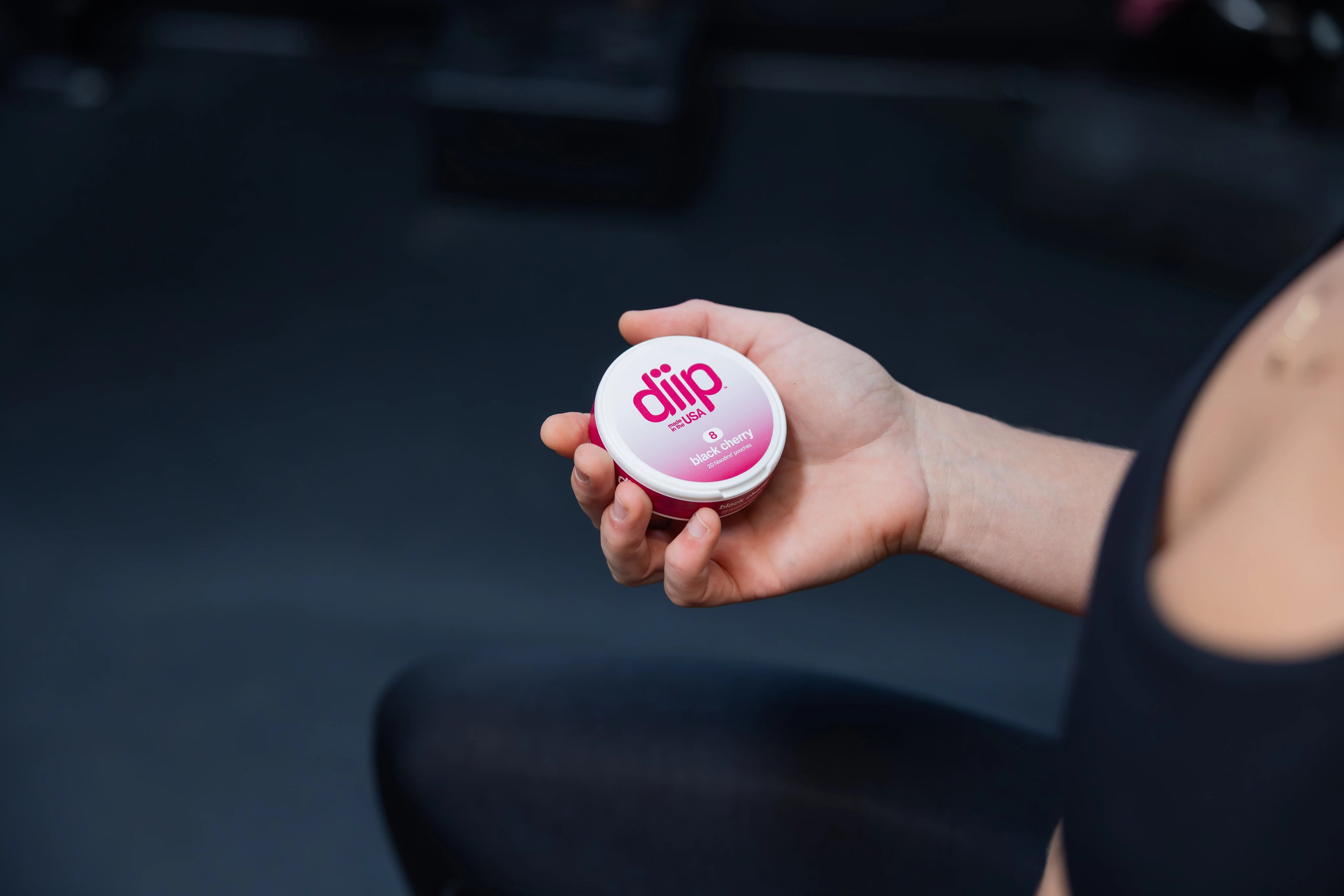 A close-up shot of a female holding a black cherry 'diip' branded nicotine-free dip pouch can in the gym