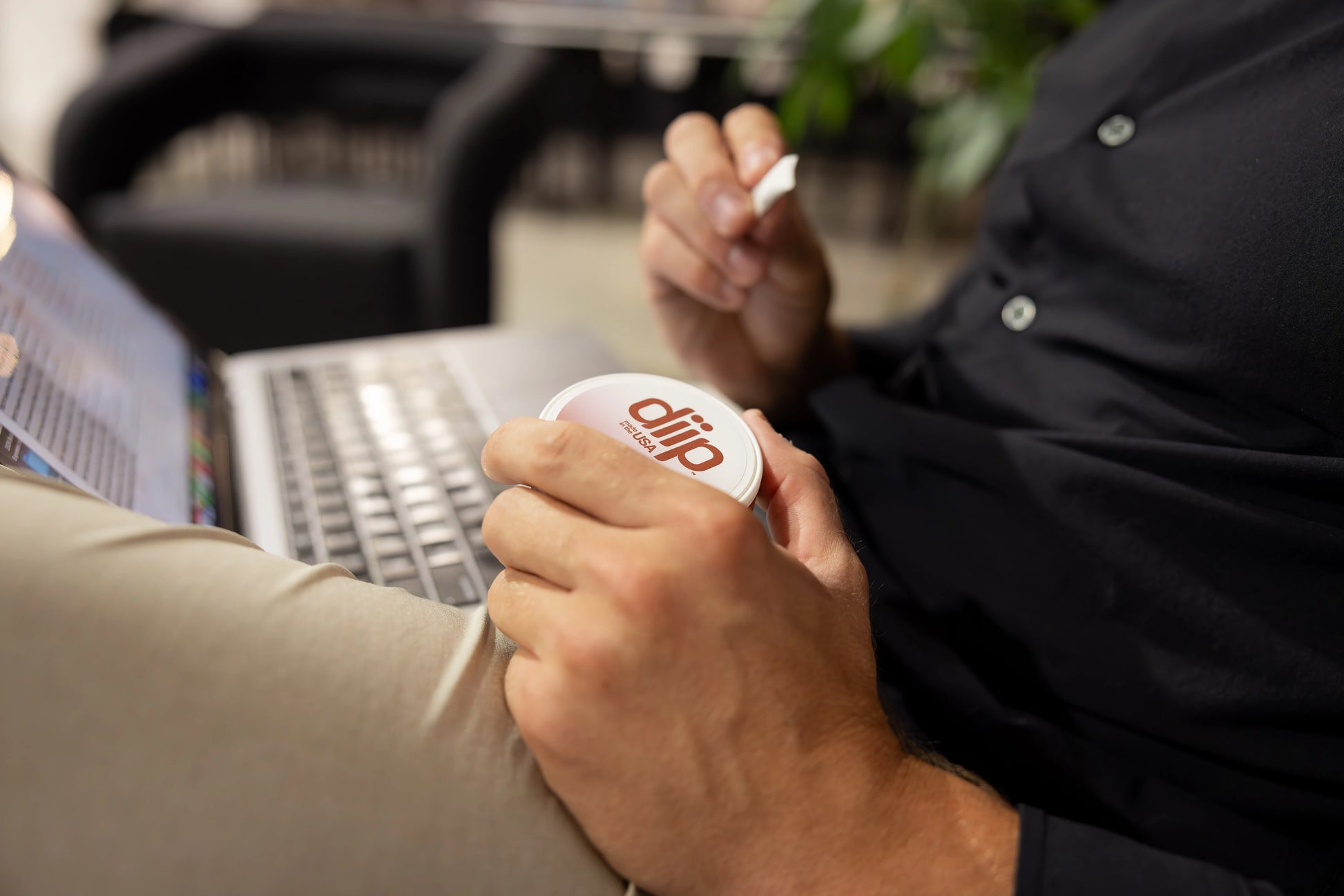 A man holding a mocha 'diip' branded nicotine-free dip pouch can while working on the computer