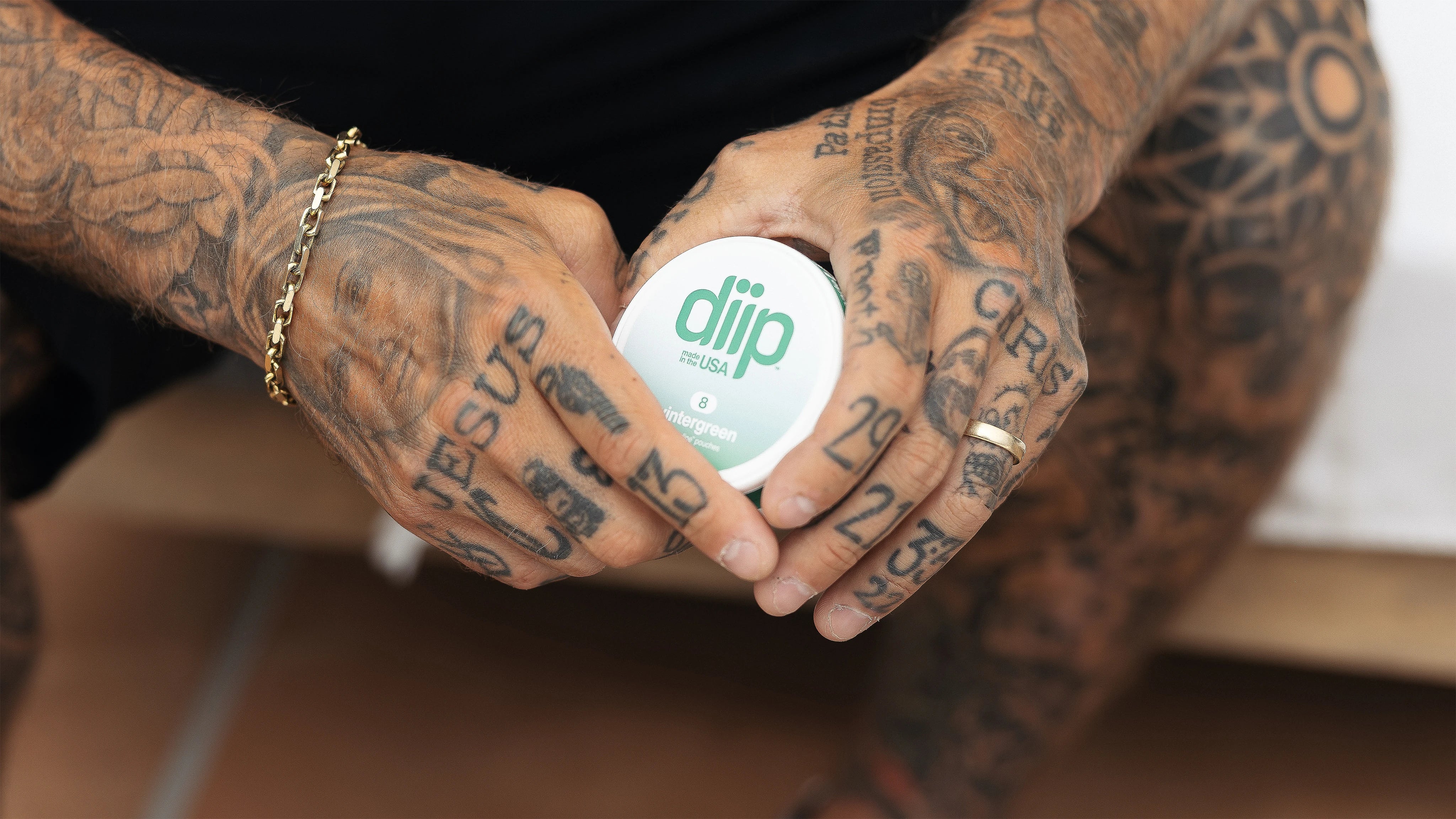A close-up shot of Ryan Sheckler sitting on a bench holding a 'diip' branded 8 wintergreen nicotine-free dip pouch can
