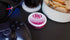 'diip' branded 8 black cherry nicotine-free dip pouch can laying on a gaming desk with a gaming controller, headphones, and snacks