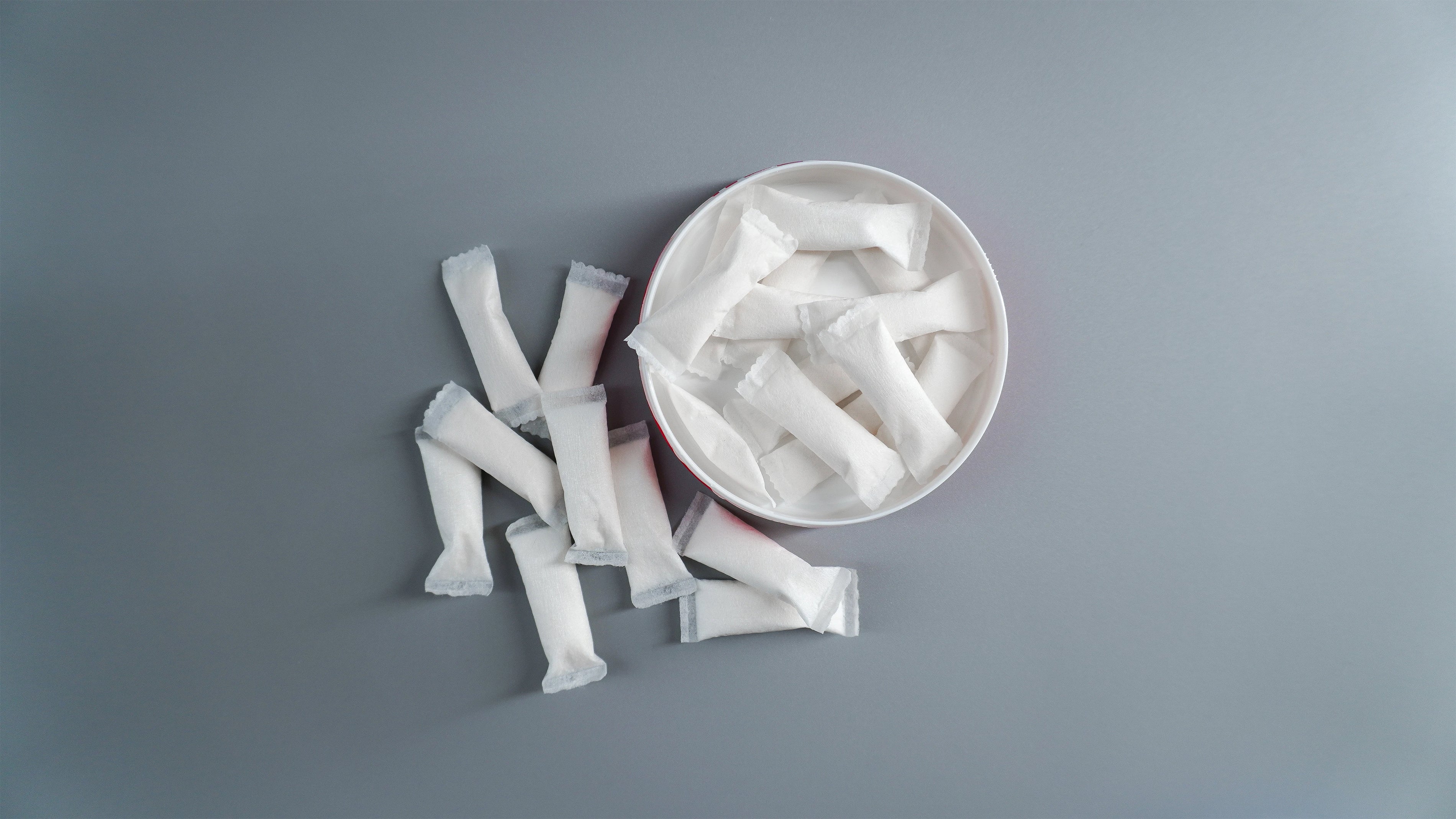 Nixodine oral pouches on a gray surface with a white can containing more nixodine oral pouches.